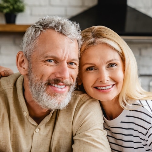 Smiling middle aged couple sitting together in a bright kitchen looking at the camera
